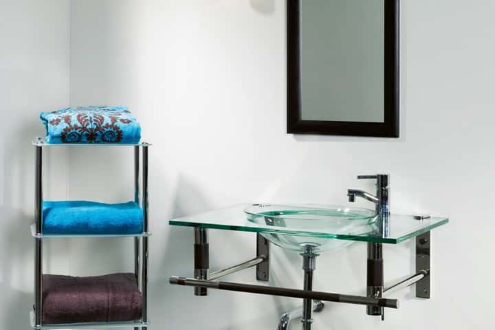 Glazen wastafelblad tegen een lichte wand, met turquoise en paarse handdoeken op een chromen rek.