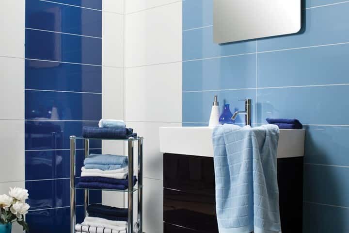 Badkamer met blauwe hoogglans wandpanelen in twee tinten, een witte wastafel en blauwe handdoeken.