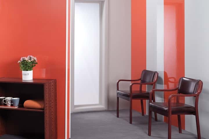 Ruimte met oranjerode hoogglans wandpanelen, een witte deur en twee donkerrode stoelen.