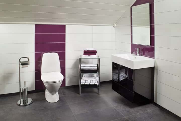 Badkamer met paarse hoogglans panelen naast witte panelen, met toilet, wastafel en spiegel.