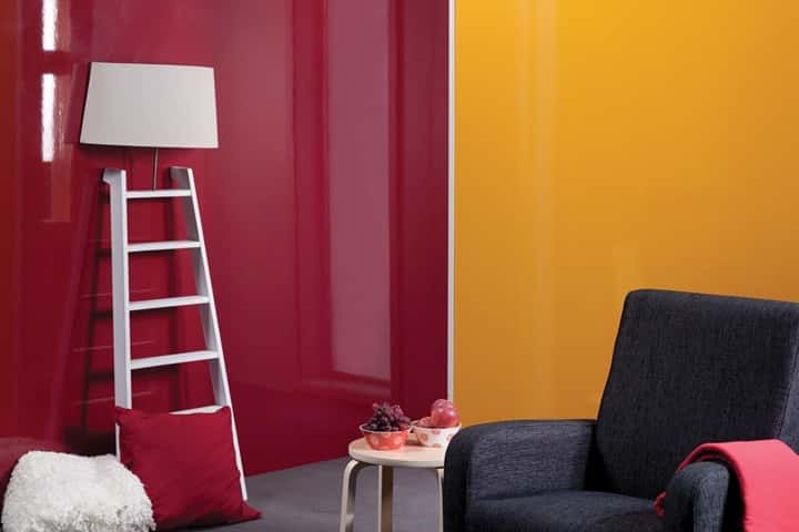 Ruimte met dieprode en okergele hoogglans wandpanelen, een witte ladderlamp en een donkere fauteuil.