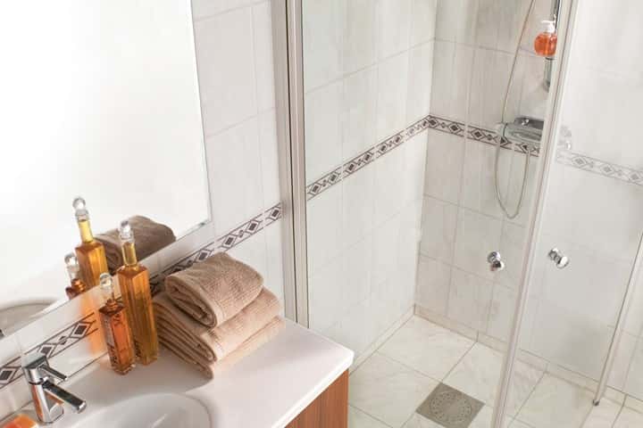 Douchehoek met glazen deur en een sierstrip met ruitmotief langs de wand, met beige handdoeken en badproducten.