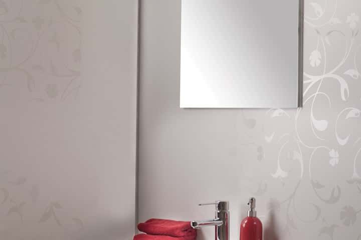 Wand met een wit bloemdessin achter een witte wastafel met rode zeepdispensers en een rechthoekige spiegel.