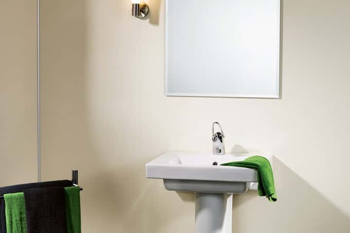 Witte staande wastafel tegen een gladde beige wand, met groene handdoeken aan een handdoekrek.