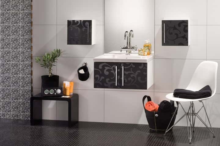 Badkamer met zwarte wandpanelen met bloemdessin naast een witte tegelwand, een zwarte wastafelkast en een witte designstoel.