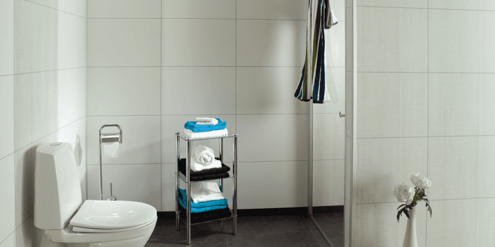 Toilet met witte tegellook-wandpanelen, een blauw badkamerrek met handdoeken en witte bloemen.